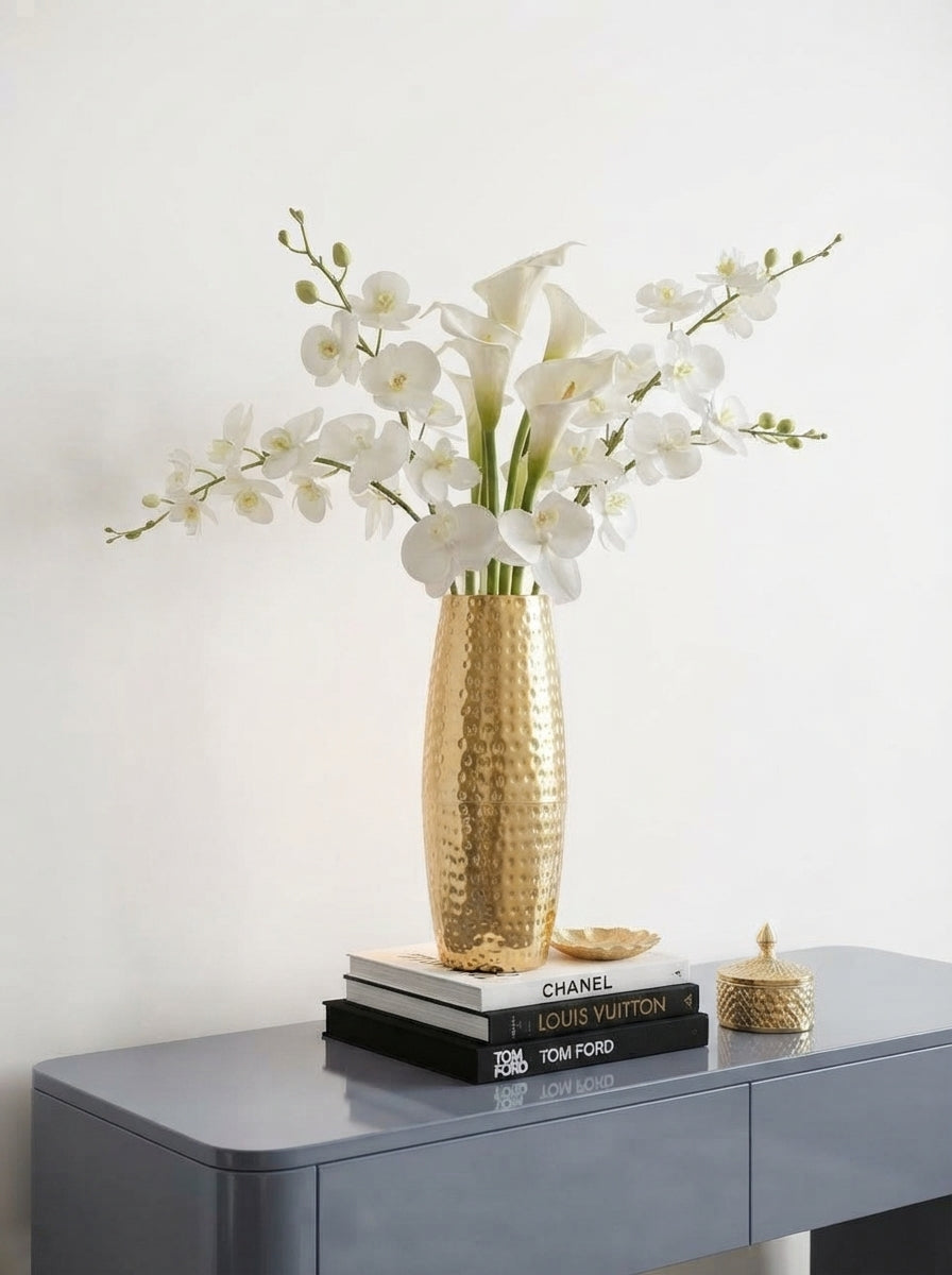 A 46 cm tall hammered metal vase with dried florals on a slate gray console table in a modern, brightly lit room.