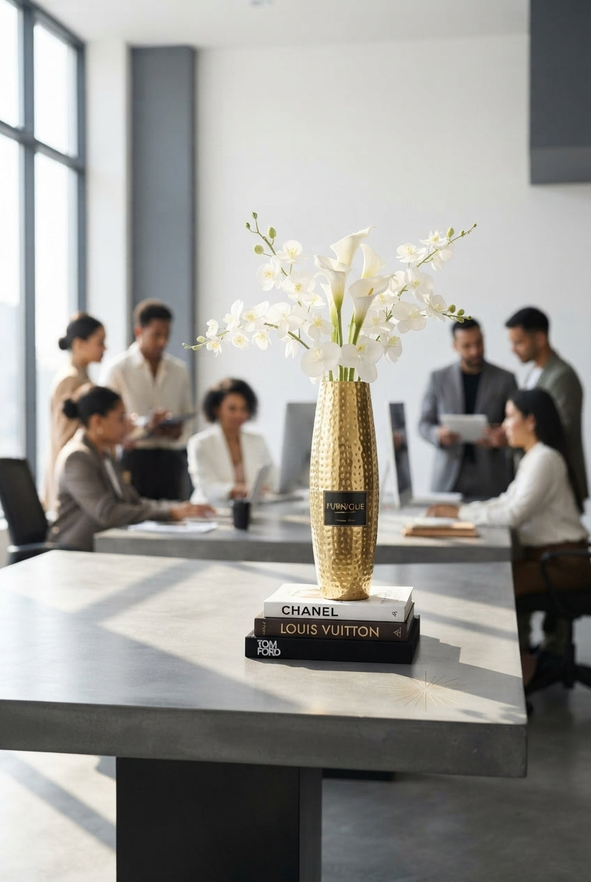 A 46 cm tall hammered metal vase with a textured surface placed on a charcoal table in a modern, light-filled design studio.